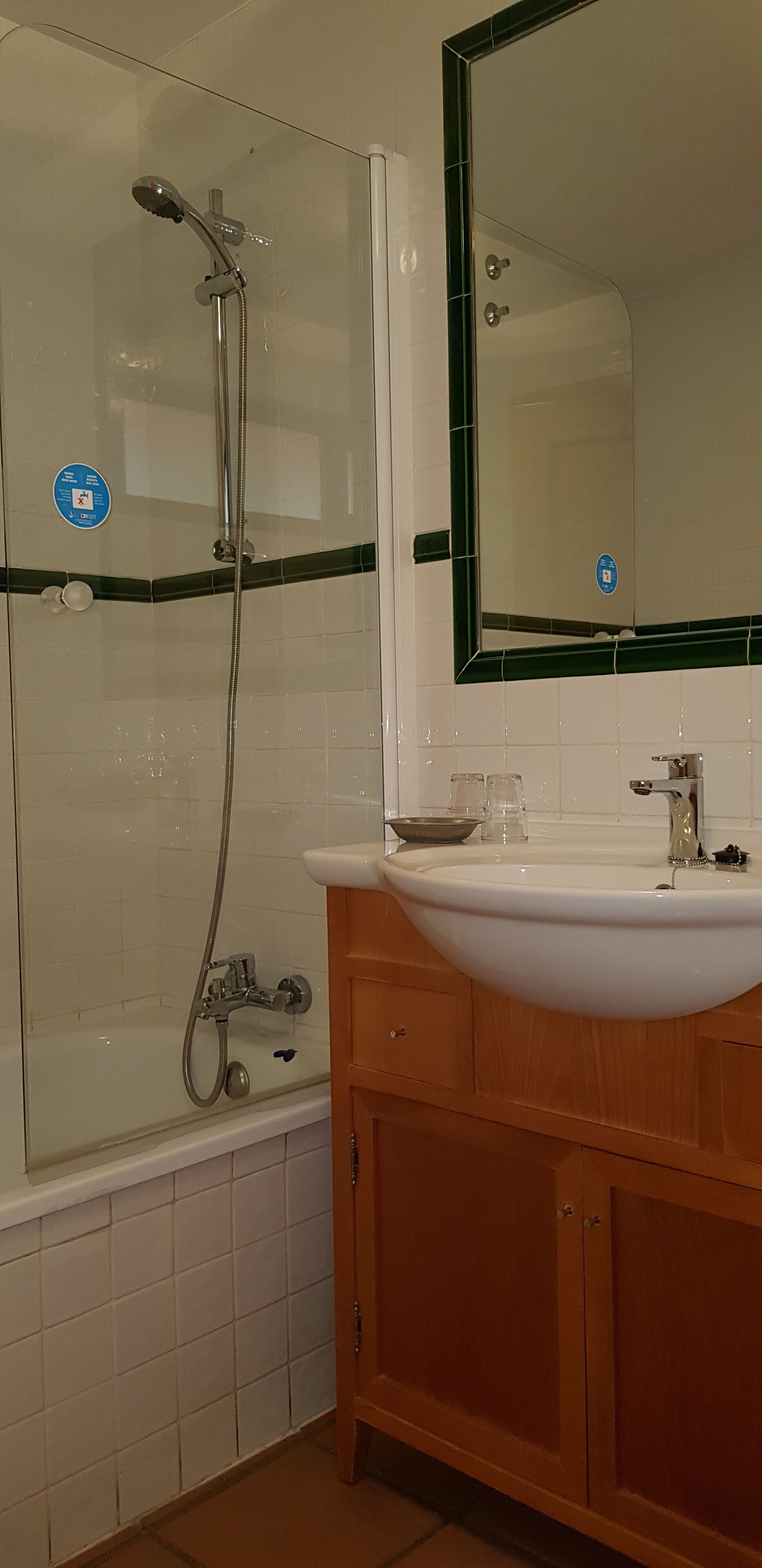 Een badkamer met een douchecabine van glas, een witte wastafel met spiegel erboven en houten kastjes.