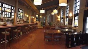 A bar area with a counter, stools, and tables. There are large windows and hanging lights. - Hotel Sara De Ur (La Cabrera)