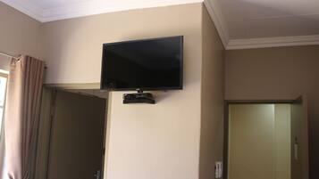 A room with a mounted television on the wall, a door, and a curtain.