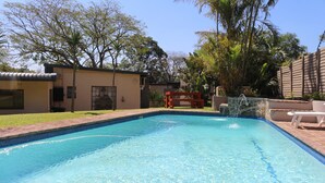 A swimming pool with clear blue water, surrounded by a brick deck and a wooden bench. - Hummingbirds Nest Guesthouse (Mbombela)