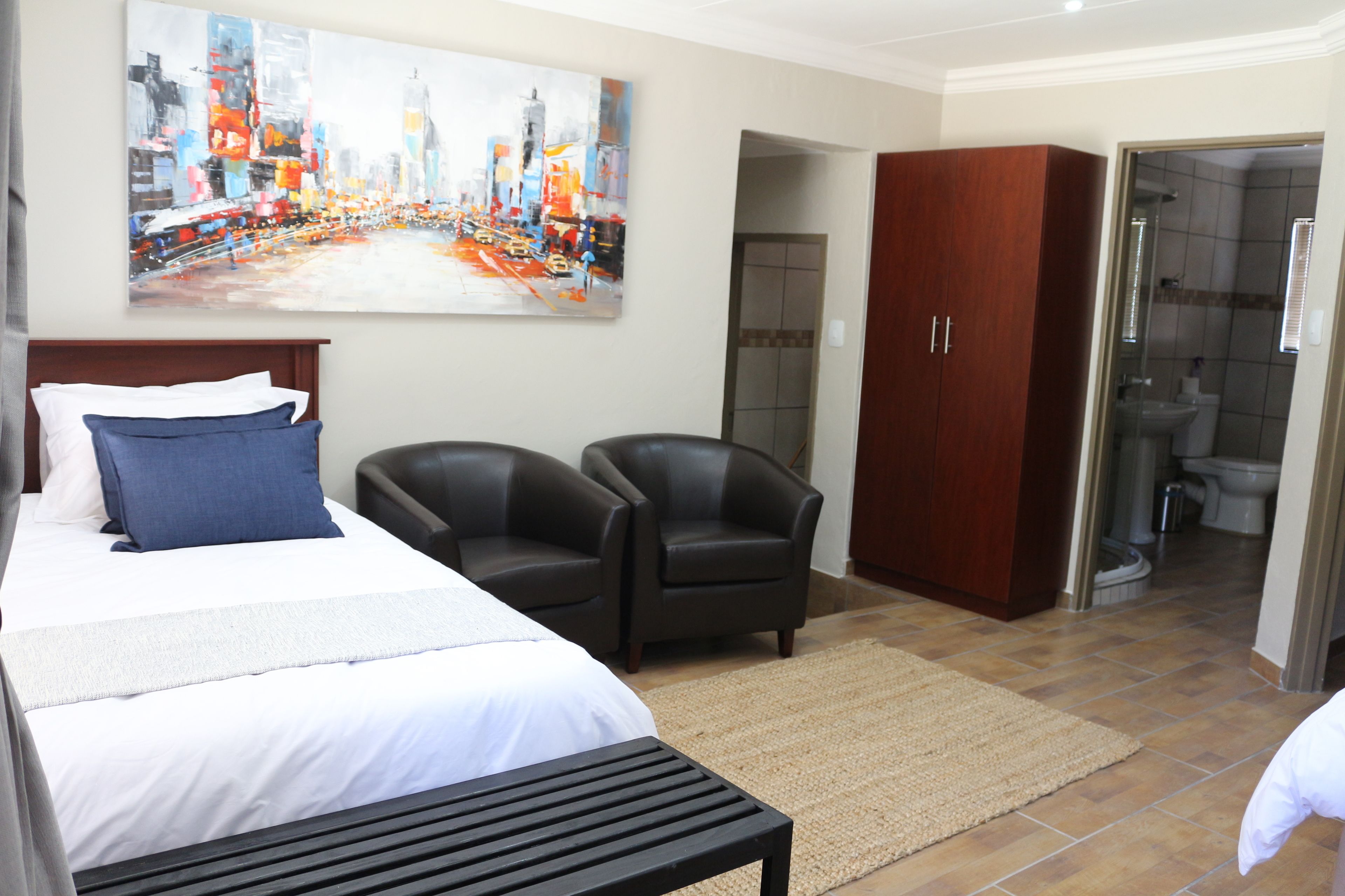 A hotel room with a bed, two armchairs, a wooden wardrobe, and a shower area.