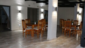 A dining area with wooden tables and chairs, white brick walls, and recessed lighting. - Hummingbirds Nest Guesthouse (Mbombela)