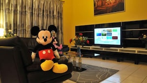 A living room with a large plush Mickey Mouse toy on a black sofa, a flat-screen TV on a stand, and a painting on the wall. - Lake Berkley - 7 Bed 5 Baths Villa (Kissimmee)