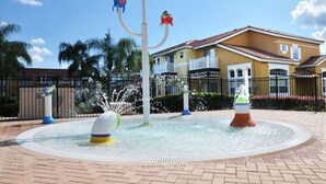 A water fountain with multiple jets and colorful fish sculptures, surrounded by a paved area and a yellow building with a red roof. - Lake Berkley - 7 Bed 5 Baths Villa (Kissimmee)