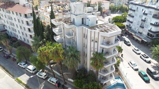 A multi-story residential building with balconies, a swimming pool, and parked cars.