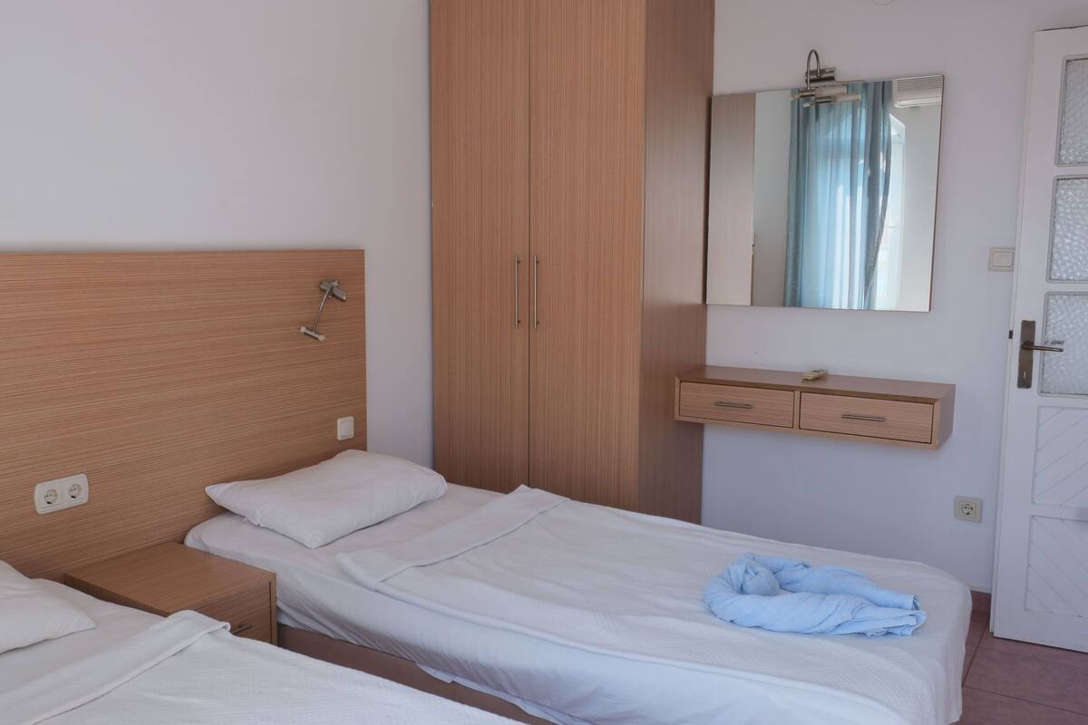 Een enkel bed met houten hoofdbord, nachtkastje, garderobe, spiegel en een deur met geëtste glazen panelen.