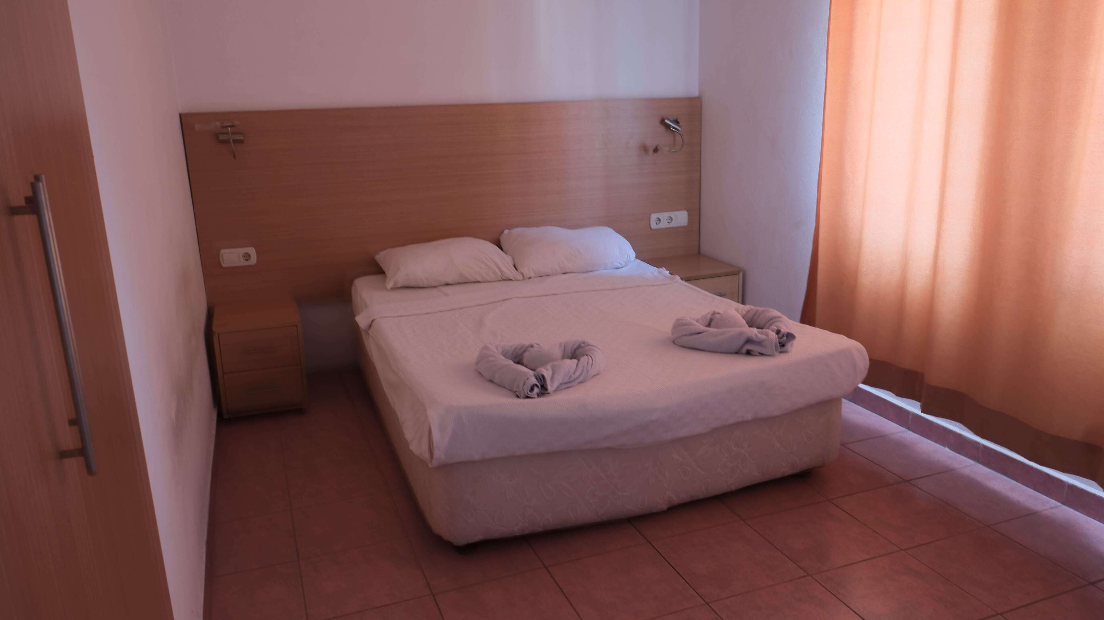 Ein Hotelzimmer mit einem großen Bett, einem Holzkopfschild, einem Nachttisch und einem Fenster mit Vorhängen.