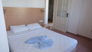 A hotel room with a wooden headboard, a bed with white linens, a towel on the bed, and a door leading to a bathroom.