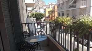 Un balcón con una mesa y sillas, vista a la calle y una montaña al fondo.