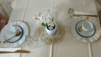 Una mesa de comedor impecable con mantel blanco, dos platos con cuencos, cucharas, una copa y un florero con flores blancas.