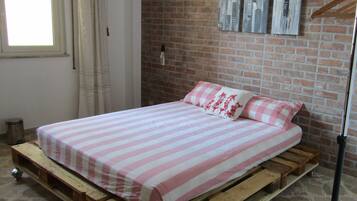 A room with a bed on a wooden platform, brick wall, and a window with curtains.