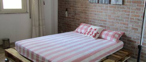 A room with a bed on a wooden platform, brick wall, and a window with curtains.