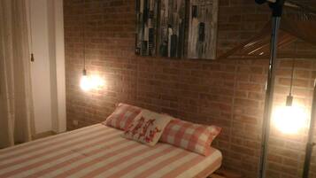 Un dormitorio con pared de ladrillo, una cama con ropa de cama a rayas y dos lámparas de pared.