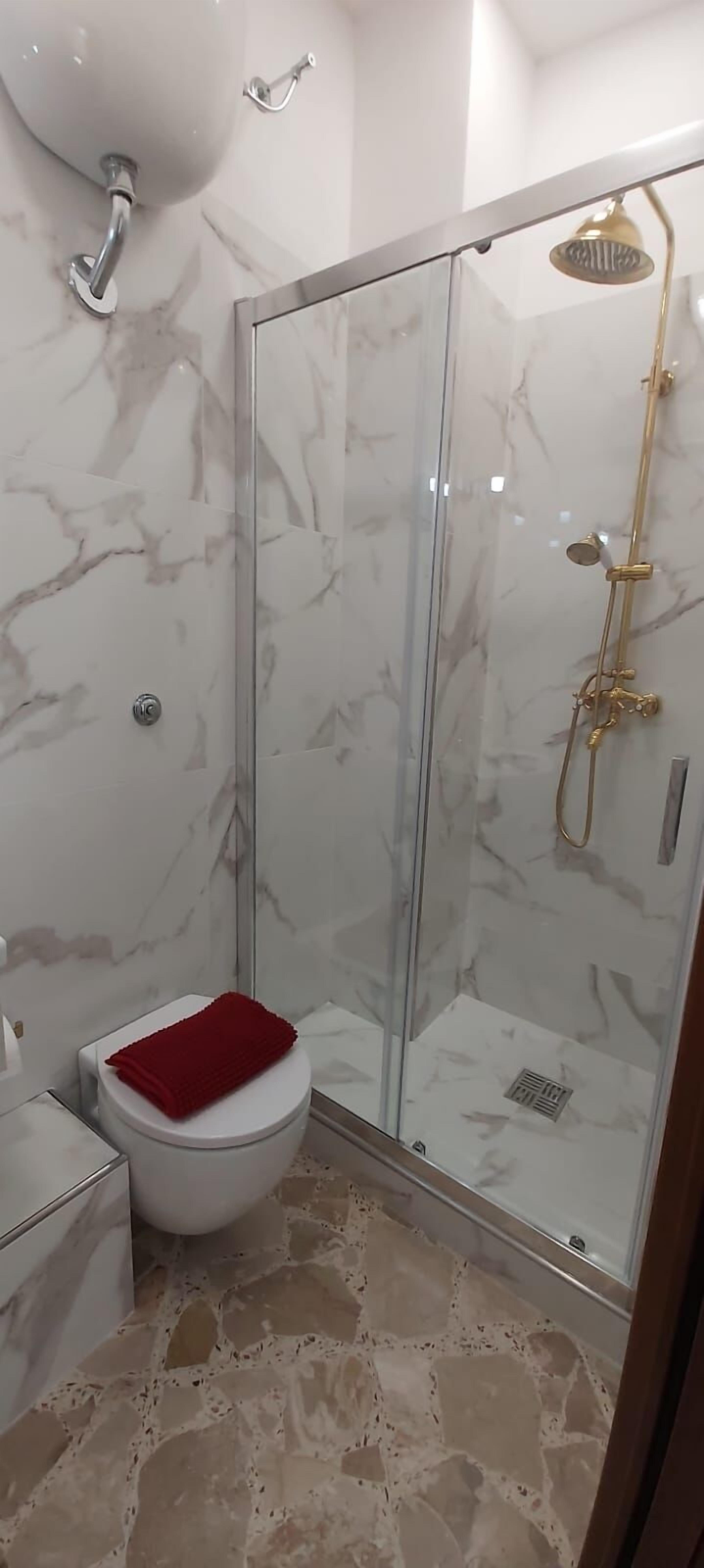 Un baño con cabina de ducha de vidrio, inodoro blanco y suelo de mármol.