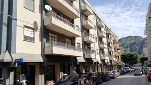 Un edificio residencial de varios pisos con balcones, autos estacionados y vista a la calle.