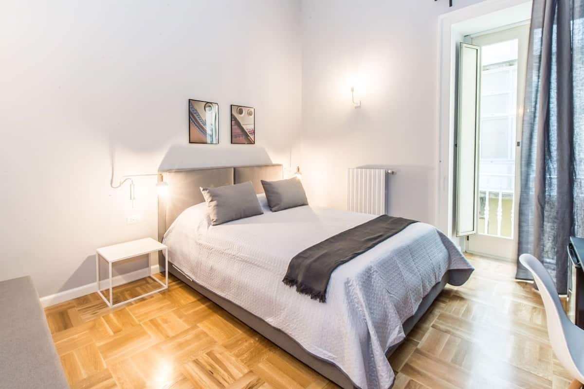 Un dormitorio con cama, mesita de noche y vistas al exterior.