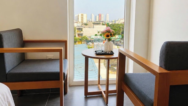 A hotel room with a large window, a small round table with a vase, and two grey upholstered chairs. - Anh Villa Hotel (Da Nang)