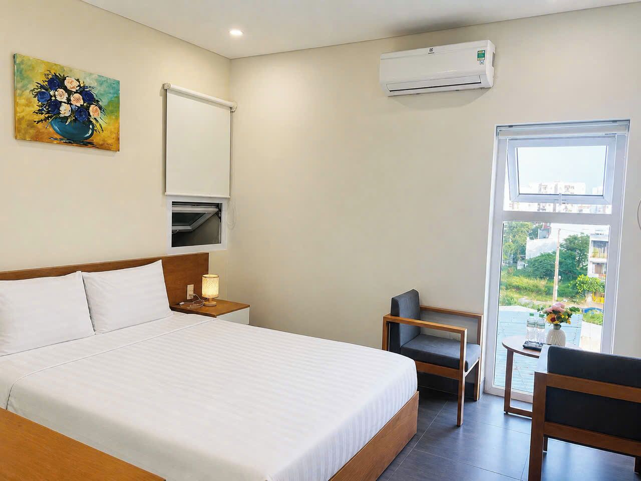 Ein Hotelzimmer mit Bett, Schreibtisch, Stuhl, Klimaanlage, Fenster und einem Bild an der Wand.