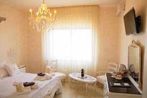 Une chambre d’hôtel avec un lit, deux chaises, une petite table avec une bouteille, un miroir et un téléviseur fixé au mur.