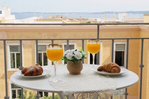 Une table sur le balcon avec des croissants et des verres de jus d’orange, un vase rempli de fleurs et, en arrière-plan, une vue sur des immeubles.