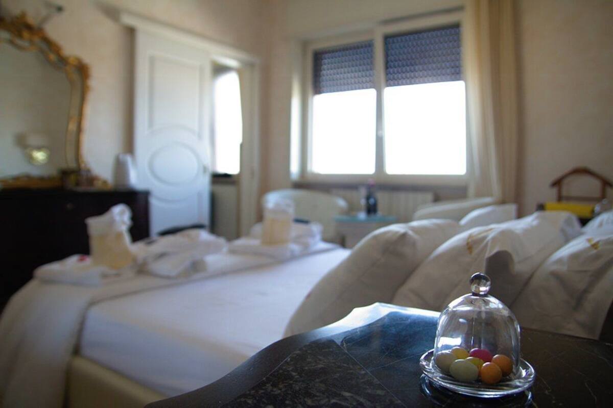 Quarto de hotel com cama, mesa de cabeceira e janela com cortinas.