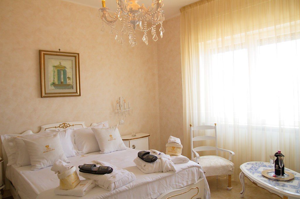 Une chambre d’hôtel comprenant un lit, une table de chevet, une chaise, une table, un lustre et une fenêtre avec des rideaux.