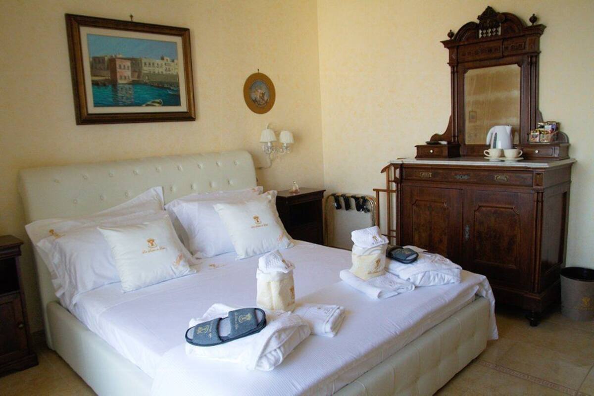 Uma cama bem arrumada com lençóis e almofadas brancos, um penteado de madeira com espelho e um quadro na parede.