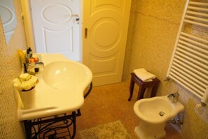 Une salle de bain avec un lavabo blanc, un bidet, un petit tabouret en bois et une serviette sur le sol.