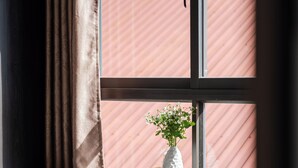 A window with a view of a red building, a vase with flowers, and a book on a table. - ELC Luxury Da Lat Hotel & Apartment (Xuan Huong - Da Lat)