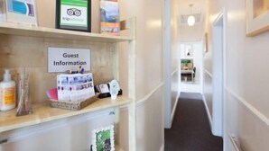 Un espace d’accueil d’hôtel avec une signalétique indiquant « Informations pour les clients », un panneau TripAdvisor et divers dépliants d’information.
