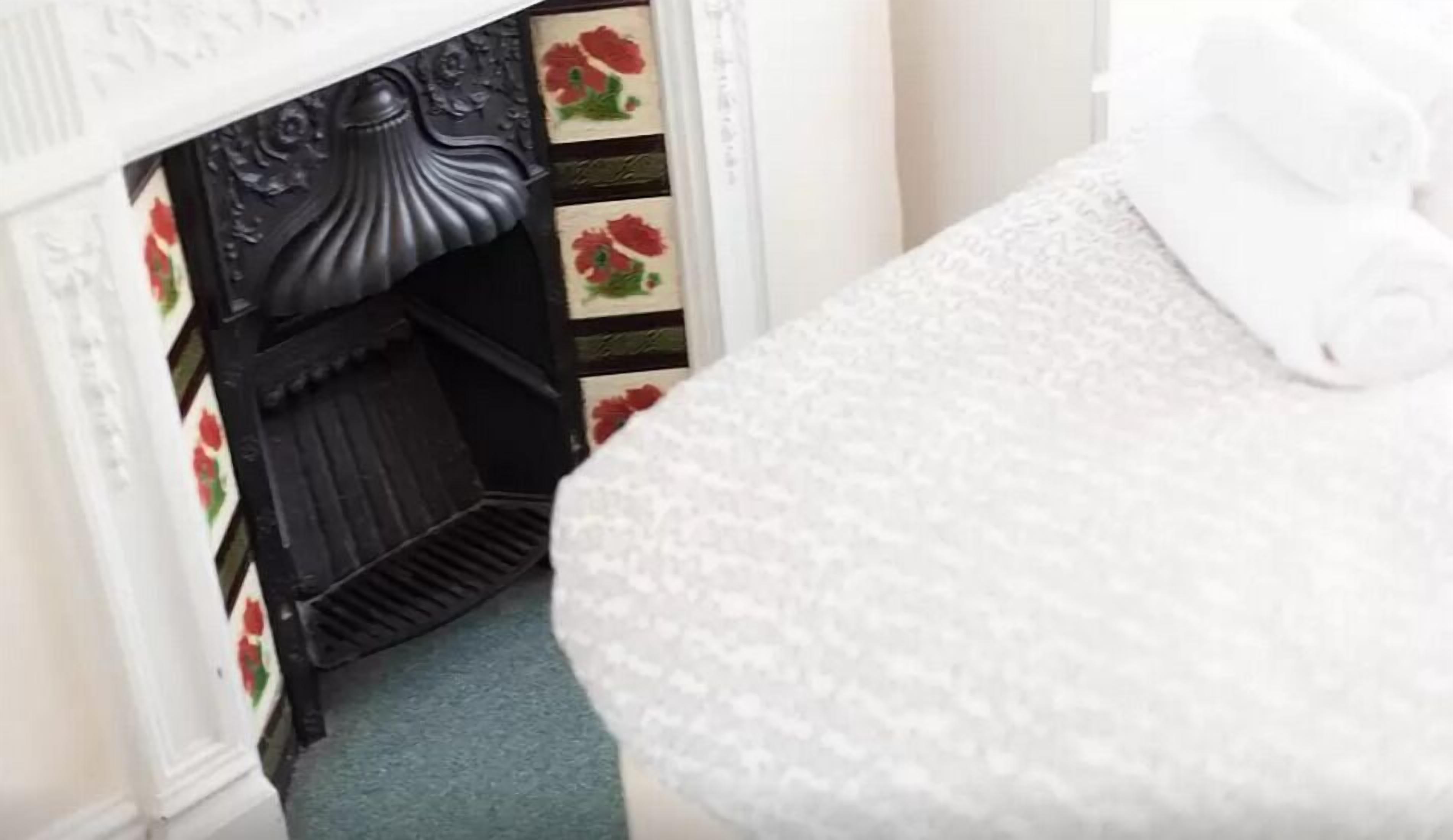 Una stanza con camino, carta da parati a motivi floreali e un letto bianco con texture.
