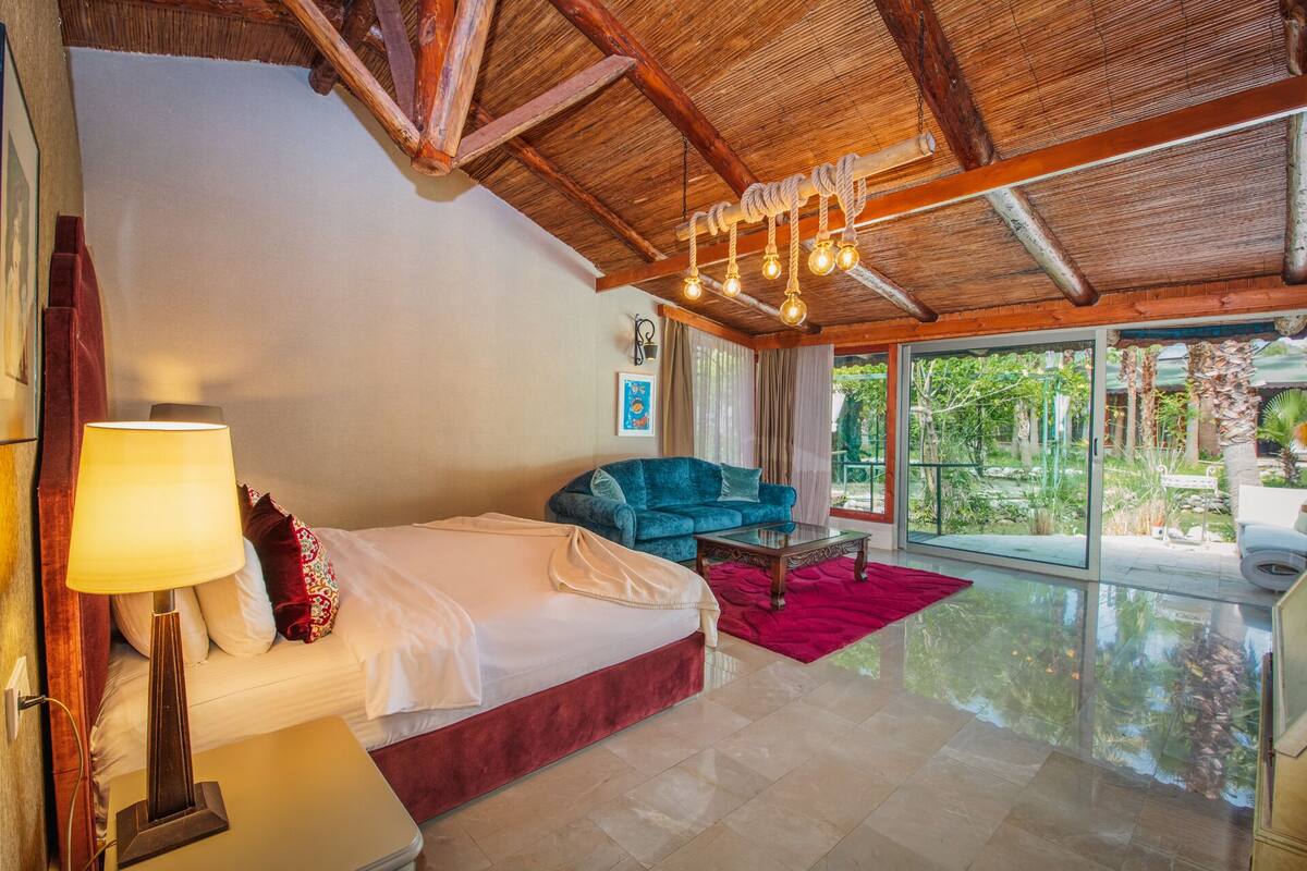 A spacious room with a bed, a blue sofa, a glass door leading to an outdoor area, and a chandelier.