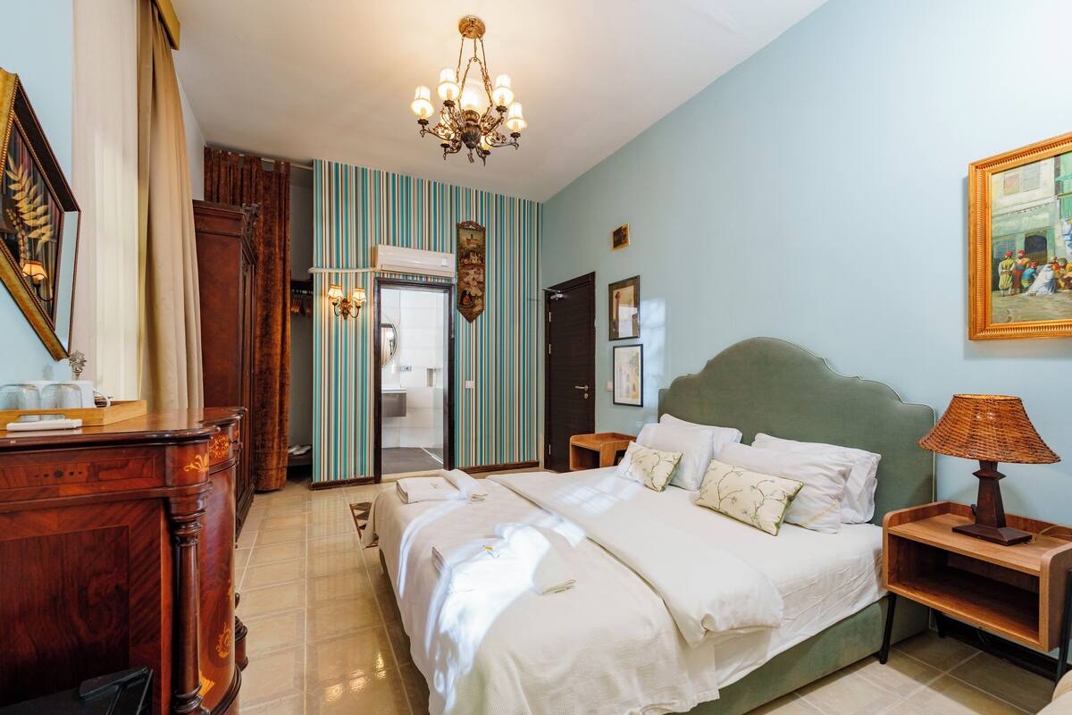 A hotel room with a large bed, a wooden dresser, a desk, and a chandelier.