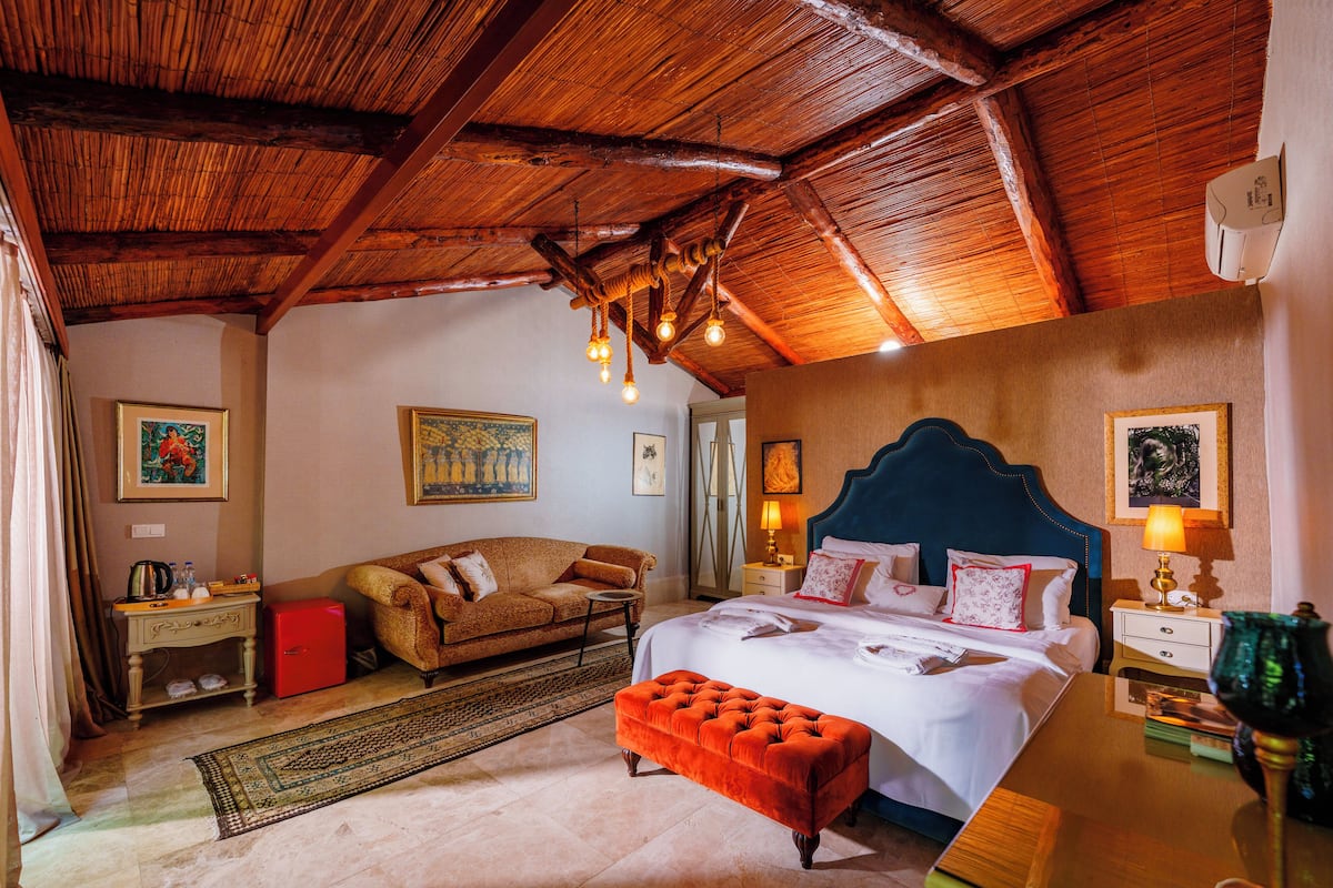 A spacious bedroom with a large bed, a sofa, a red cabinet, and a wooden ceiling.
