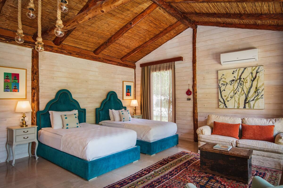 A room with two beds, a sofa, a patterned rug, and a ceiling with exposed beams.
