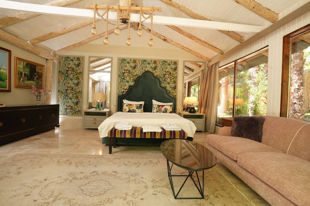 A spacious bedroom with a large bed, a sofa, and a dining table.