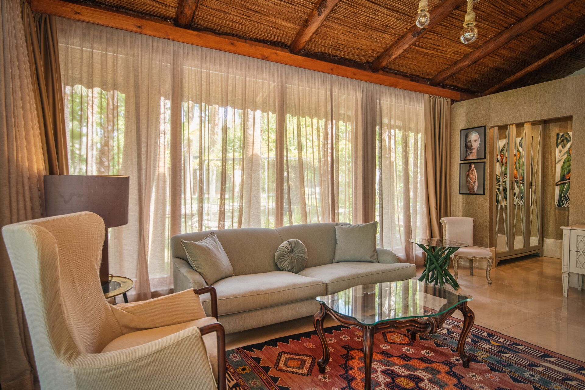 Sala de estar com sofá, poltrona, mesa de centro de vidro e tapete estampado.