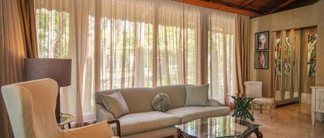 Sala de estar com sofá, poltrona, mesa de centro de vidro e tapete estampado.