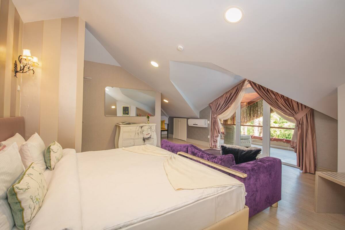 A bedroom with a large bed, a dresser, a vanity, and a window with curtains.