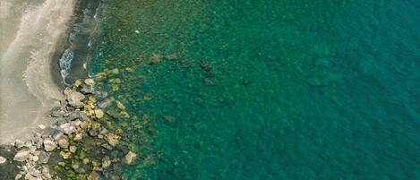 Vue aérienne d’une plage aux eaux turquoise et limpides, bordée d’une côte rocheuse et d’une plage de sable.