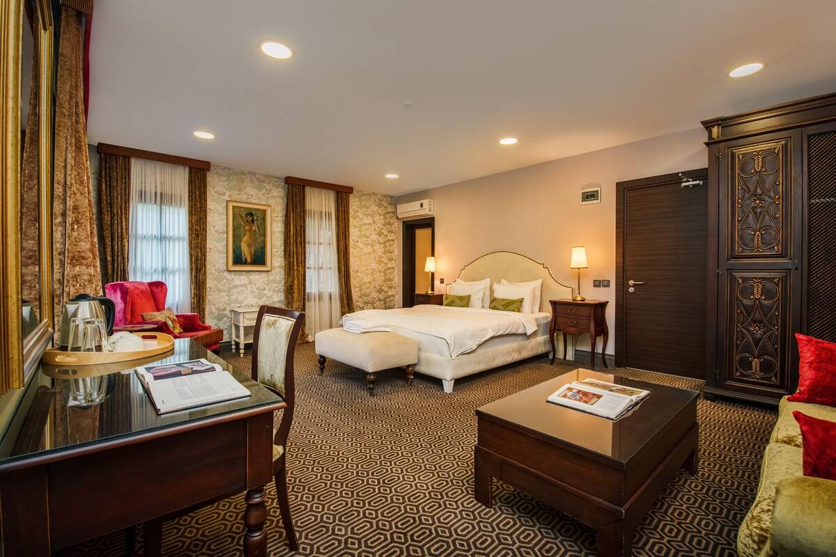 A hotel room with a bed, bedside tables, a desk, a chair, a wardrobe, and a patterned carpet.
