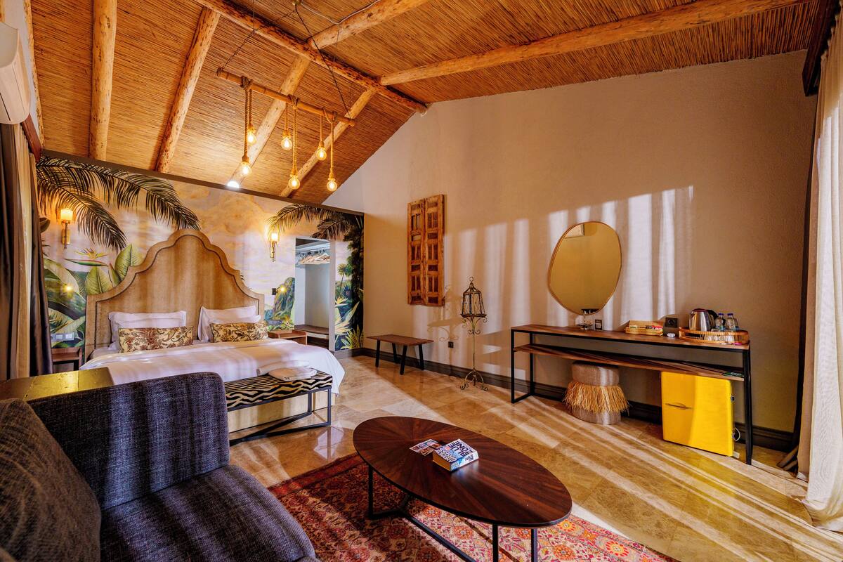 A room with a bed, a sofa, a small table, a desk with a mirror, and a yellow cabinet.