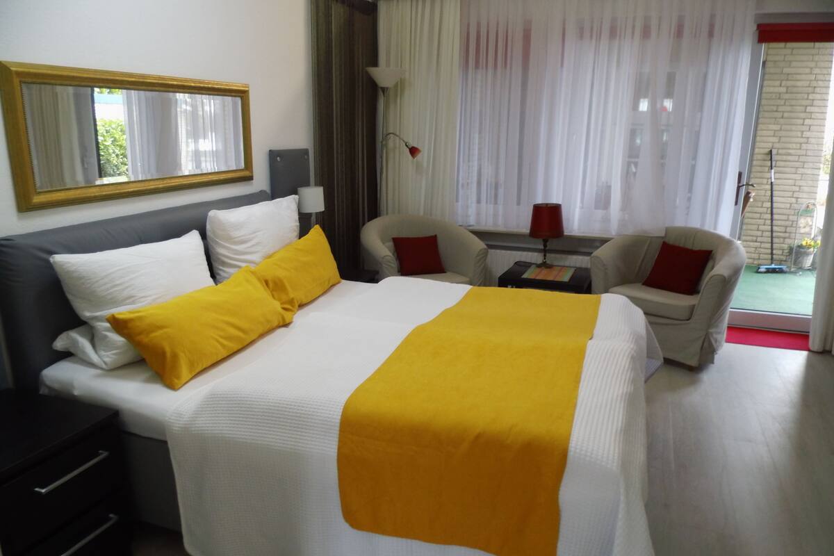 A hotel room with a large bed, two armchairs, a small table, and a mirror.