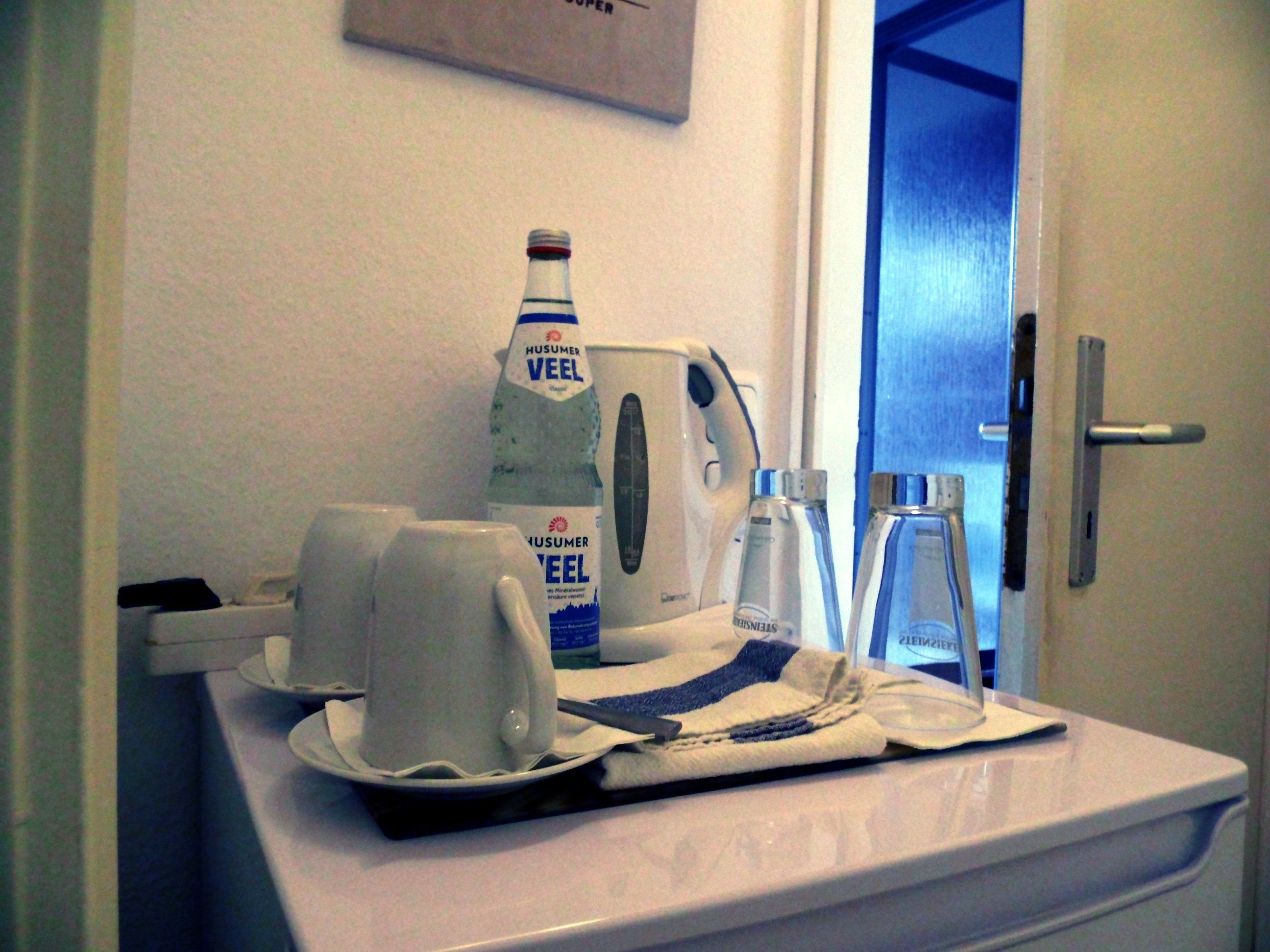 A hotel bathroom with a sink, a mirror, a towel, and toiletries including a bottle of HUSUMER VEEL and a bottle of STEINHEISER.