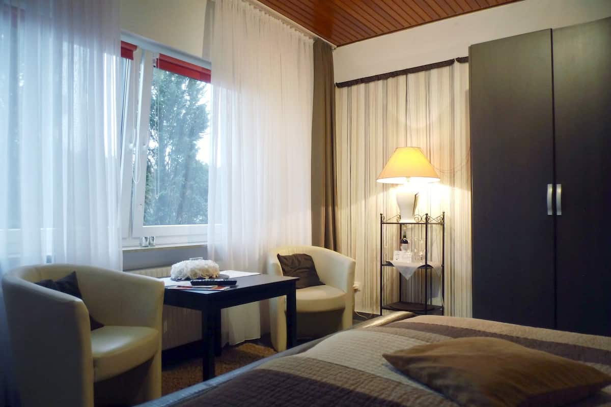 A hotel room with a bed, two chairs, a small table, a lamp, and a wardrobe.