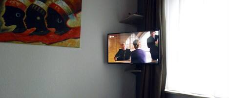 Habitación de hotel con una cama, televisor en la pared y un cuadro sobre la cama.
