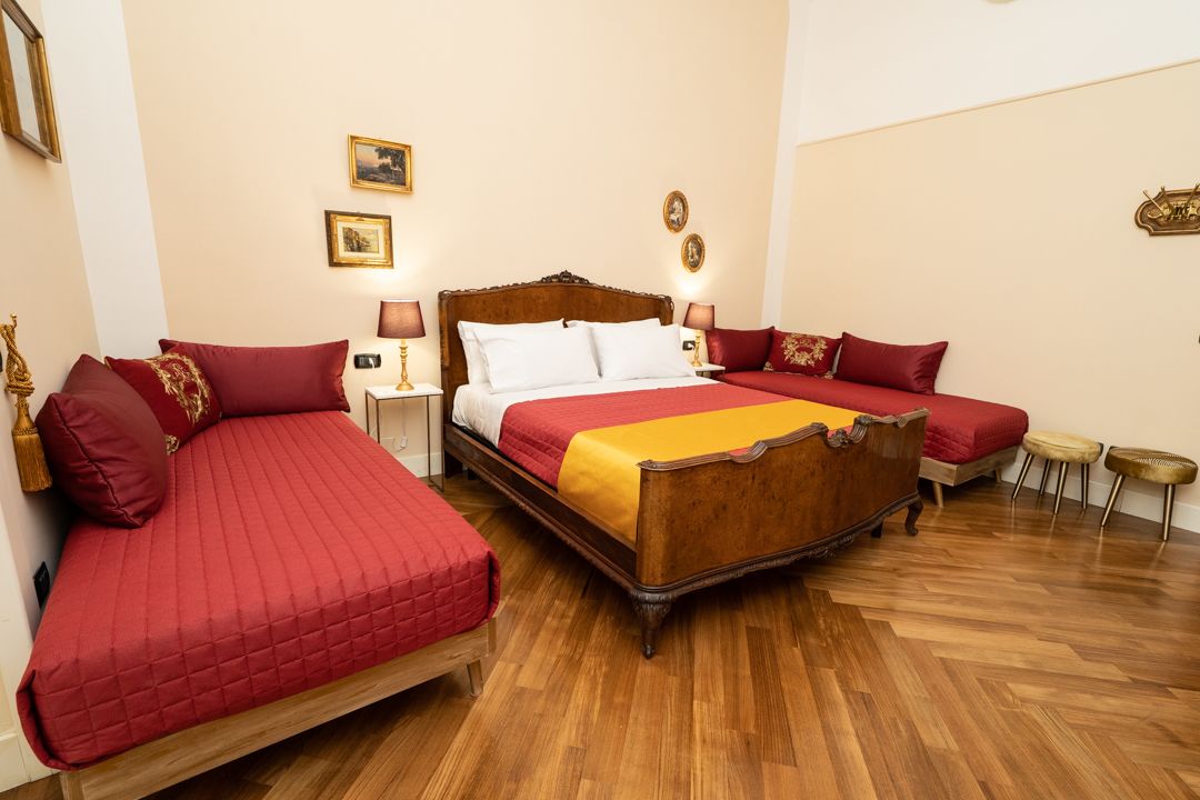 Un dormitorio con una cama grande, dos camas más pequeñas, suelo de madera y cuadros colgados en la pared.