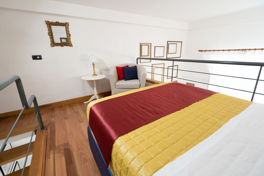 Una habitación de hotel con cama, una silla, una mesita y una barandilla.