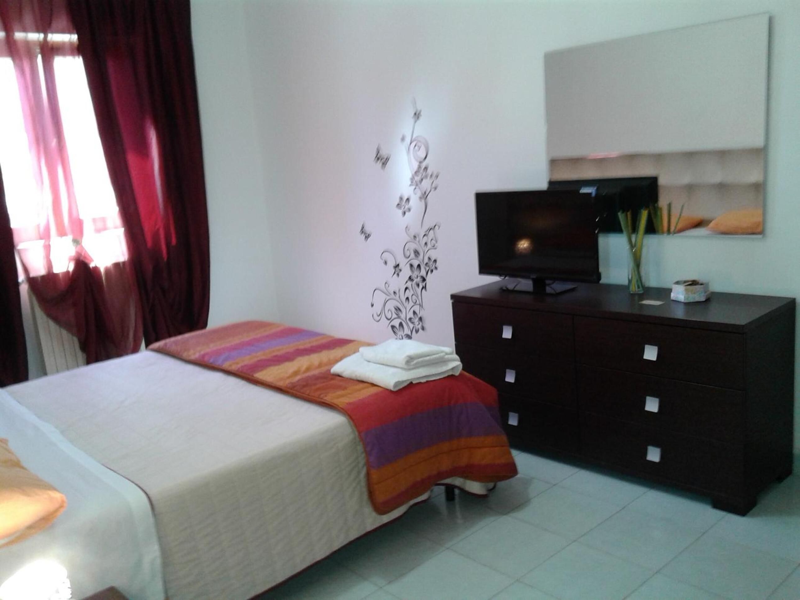 Un dormitorio con cama, cómoda, televisor y decoración en la pared.