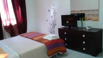Un dormitorio con cama, cómoda, televisor y decoración en la pared.
